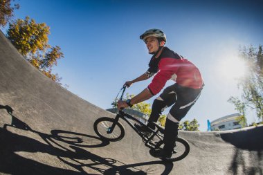 Güneşli bir günün tadını çıkarırken BMX bisikleti süren genç bir erkek. Arka planda güneş olan düşük profilli balık gözlü fotoğraf