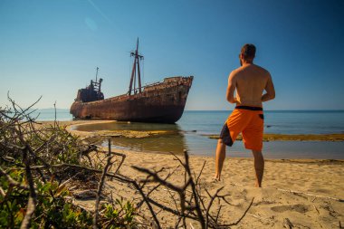 Yunanistan 'ın Gythio kentinde Dimitrios' un gemi enkazını izleyen biri. Güneşli bir günde kumlu bir sahilde kısmen çökmüş paslı ve metal bir gemi enkazı. Yunanistan 'ın ünlü gemi enkazı.