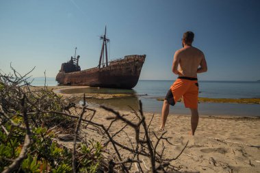 Yunanistan 'ın Gythio kentinde Dimitrios' un gemi enkazını izleyen biri. Güneşli bir günde kumlu bir sahilde kısmen paslı bir metal gemi enkazı çürüyor. Yunanistan 'ın ünlü gemi enkazı.