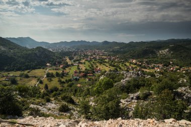 Karadağ 'ın eski başkenti Cetinje' nin Panoraması. Çetince 'nin yemyeşil tepelerde ve ormanlarda saklanan evlerine doğru bakın. Ön planda kayalar var..