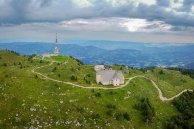 Bir yaz günü Koroska bölgesindeki Urslja gora Tepesi veya Plesivec 'in insansız hava aracı panoraması. Görülebilir çimenler, Aziz Ursula Kilisesi ve üzerinde Pohorje dağları olan televizyon anteni..