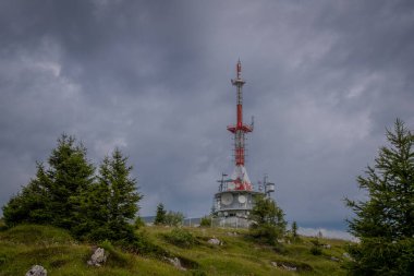 Slovenya 'da Urslja gora' nın tepesinde ağaçlar ve bulutlarla çevrili bir televizyon kulesi veya anten..