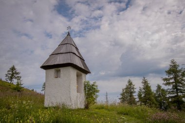 Slovenya 'nın Urslja Gora dağında, yemyeşil, çiçek ve kalın beyaz bulutlarla çevrili küçük beyaz bir Hıristiyan şapeli..