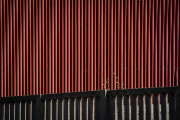 Red metal wall texture of a factory, with a concrete wall in front of it. 3D effect of factory wall.