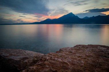 Garda Gölü 'nde sakin bir an. Önünde taşlar ve zengin dağların ardında gün batımı. Göldeki sükunet kavramı.
