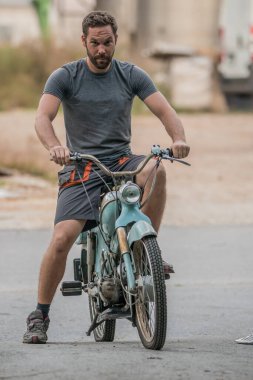 1950 ya da 50 'lerden kalma eski mavi bir motosiklet ya da scooter' ın ön görüntüsü. Asfalt park yerine park etmiş eski model bir motosiklet ve üzerinde bir adam var..