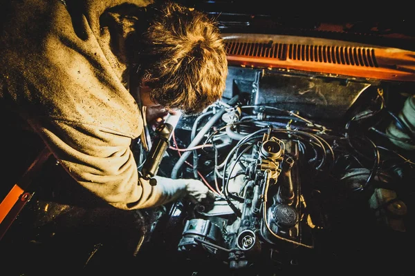 A man fixing an engine of a car at night. Vintage car being repaired during a night time. Bad timing for a car repair. Concept of a bad luck with a car.