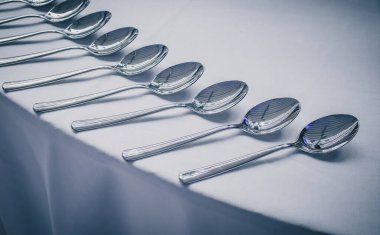 Bir gala etkinliğinde ya da yemek servisinde bir sıra gümüş kaşık bir masanın kenarında sıraya dizilmeyi bekliyor. Kaşıklar masada..