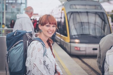 Tramvay ya da tren beklerken tramvay platformunda duran bayan turist ya da gezgin. Tren istasyonunda mavi sırt çantalı genç bir kadın, tren bekliyor ve gülümsüyor..