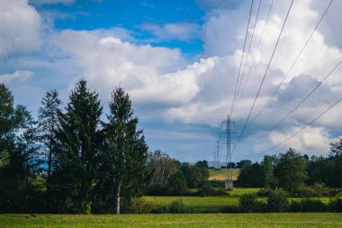 Elektrik hatları tarladan geçiyor ve bulutlu bir zemin üzerinde ağaçlar var. Uzun mesafeler üzerinden elektrik taşıma.