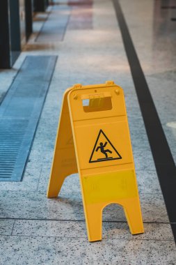 Mermer zemini olan bir koridorda sarı kaygan bir tabela var. Bölgedeki kaygan ıslak zemin hakkında insanları bilgilendiriyor..