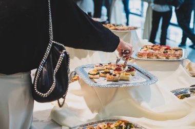 Bir kadın oteldeki bir ziyafette gümüş tabaktan maşa kullanarak küçük bir sandviç alıyor..