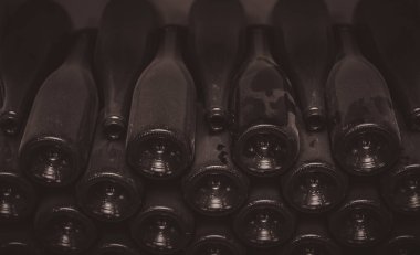 Şarap mahzeninde tozlu, eski şarap şişeleri üst üste yığılmış. Kirli ve tozlu şarap şişelerinin bir araya toplanmış yatay resmi..