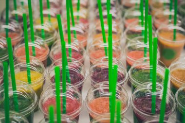 İçinde farklı renklerde meyve suları olan bir sürü plastik kutu ya da bardak. Meyve suları seçebileceğim bir masada. Plastik bardaklarda smoothie koleksiyonu.