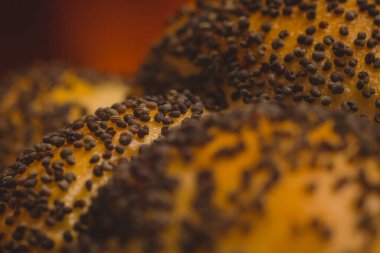 Makro, ekmeğin üzerinde haşhaş tohumu ya da arka planda ateş izi olan simit fotoğrafını kapat. Ekmek ve fırın zemininde haşhaş tohumlarının detaylı fotoğrafı.