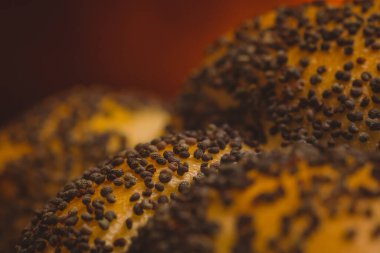 Makro, ekmeğin üzerinde haşhaş tohumu ya da arka planda ateş izi olan simit fotoğrafını kapat. Ekmek ve fırın zemininde haşhaş tohumlarının detaylı fotoğrafı.