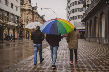 Aralarında gökkuşağı renkli şemsiyeli üç adam şemsiyelerle yürüyor. Yağmurlu bir günde Slovenya 'nın Ljubljana kentinde gökkuşağı şemsiyesiyle dolaşmak.