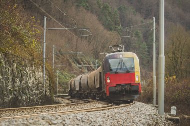 Önünde modern bir lokomotifi olan Avrupa tarzı bir yük treni vadideki bir virajda tahıl ve diğer malları taşıyor. Sonbahar ayarı.