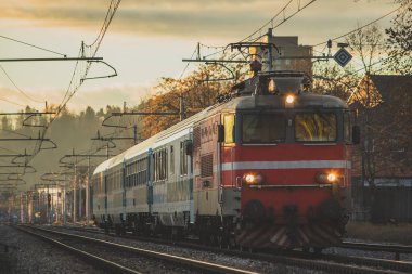 Akşam saatlerinde, düz bir yolda, önünde eski bir lokomotifle Avrupa tarzı bir yolcu treni. Romantik tren yolculuğu günbatımında.