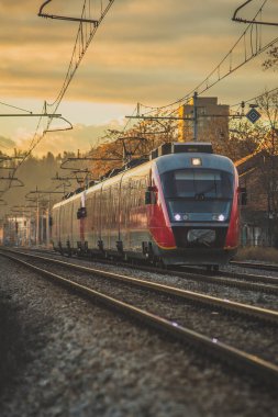 Akşam saatlerinde şehir ortamında düz bir yolda Avrupa tarzı kırmızı yolcu treni. Gün batımında romantik tren yolculuğu. Romantik akşam seyahati.