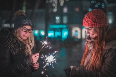 Ellerinde maytap olan iki genç kadın, şehrin merkezinde Noel ışıklarının altında bir akşam geçiriyorlar. Soğuk kış atmosferi ve şehir dışında keyif. Maytaplara odaklan..