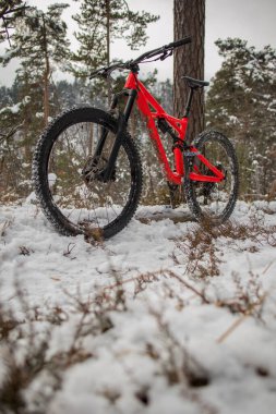 Enduro 27,5 dağ bisikleti. Kırmızı renkte. Soğuk bir kış gününde tek bir pistte dinleniyor. Soğuk ve karlı havada ekstrem spor ya da dağ bisikleti kavramı. Kışın dışarıda..