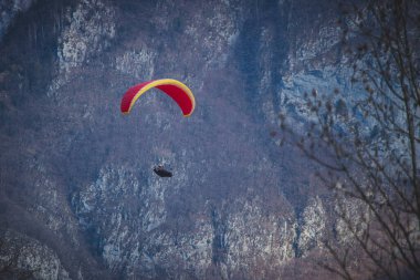 Kırmızı paraşütlü bir paraglider arka planında resim gibi bir dağ zeminiyle Slovenya 'nın Kanin kentine iniyor. Bir paraşütle dağlarda uçmak.
