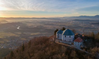 Slovenya 'nın Ljubljana kenti yakınlarındaki Smarna gora ya da Saint Mary tepesinin sabah hava manzarası, gün doğumunda çekildi. Sabah güneşi altında görünen geniş Ljubljana manzarası ve ön planda da kilise..