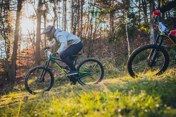 極端なマウンテンバイクは フルフェイスヘルメット ゴーグル フルサスペンション自転車で下り坂に乗る 後ろから秋の太陽 別のバイカーは彼を追いかけている — ストック写真