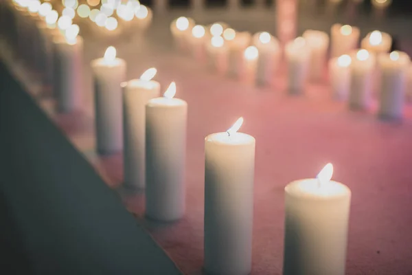 Row of white candles, aisle made out of white lit candles, with a slightly red background.