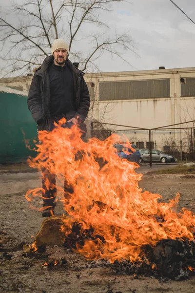 A man is burning a fire out of paper in an open space and watching. Burning paper waste in residental or industrial environment. Pollution with burning paper.