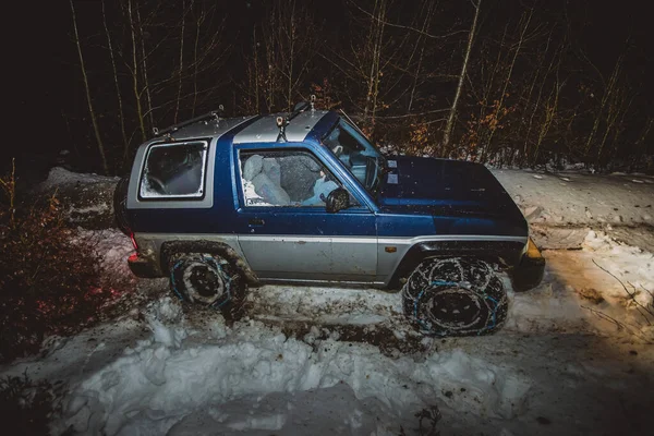 吉普车在大雪中滑行 银色和蓝色越野车 使用雪链在夜间要求陡峭的雪地上行驶 — 图库照片