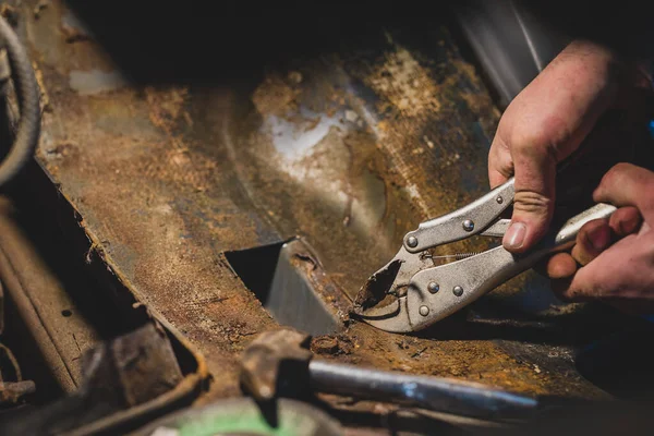 車の車体の下から古い錆びた金属を除去するためにペンチを使用して見た男の手 車と頑固な金属片の復元 — ストック写真