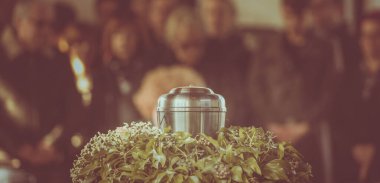 Cenaze töreninin arka planında yas tutan insanların külleri olan metal bir vazo. Bir hayatın sonunda kederli bir an. Vazodaki birine son bir veda..