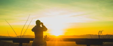 Tepenin tepesinde, güneşin doğuşundaki bir güneşin fotoğrafını çeken kadın yürüyüşçü. Zirveye erken gidip fotoğraf çekeceğim. Erken ve güzel doğa kavramı.