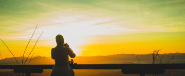 Tepenin tepesinde, güneşin doğuşundaki bir güneşin fotoğrafını çeken kadın yürüyüşçü. Zirveye erken gidip fotoğraf çekeceğim. Erken ve güzel doğa kavramı.