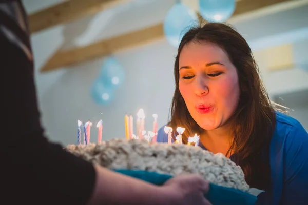 若い白人のブルネットの女性がろうそくの誕生日ケーキにろうそくを吹き消しました 屋内パーティーで女の子のためのおいしい誕生日プレゼント — ストック写真