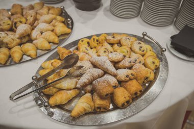Bir konferansta sergilenen kruvasan ve diğer hamur işleri ya da kahvaltı yemeğinin bir parçası olarak verilen bir ziyafet. Beyaz bir masada kruvasanlar.