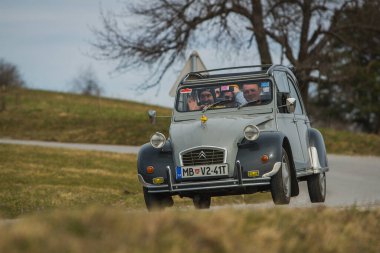 JANCE, SLOVENIA, 16.3.2019: Gri bir vintage Citroen 2CV arabası, içinde mutlu yolcuların bulunduğu bir kır yolunda virajdan çıkıyor.