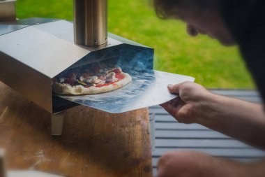 Adam paslanmaz çelikten yapılmış taşınabilir fırından taze ve leziz bir pizza çekiyor. Açık hava pizza partisi..