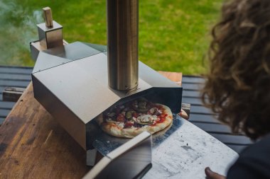 Adam paslanmaz çelikten yapılmış taşınabilir fırından taze ve leziz bir pizza çekiyor. Açık hava pizza partisi..