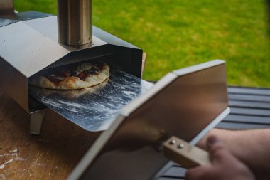 Adam paslanmaz çelikten yapılmış taşınabilir fırından taze ve leziz bir pizza çekiyor. Açık hava pizza partisi..