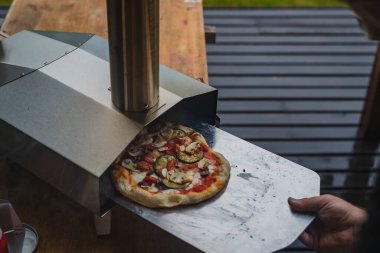 Adam paslanmaz çelikten yapılmış taşınabilir fırından taze ve leziz bir pizza çekiyor. Açık hava pizza partisi..