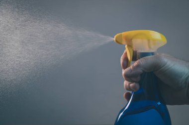 Temizlemek ve işletmek için çıplak elle bir sprey şişesi tutuyor. Şişeden damlalar her yere püskürtülüyor. Operasyonel plastik sprey şişesinin yan görüntüsü.