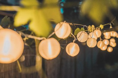 Geceleri ahşap sazdan bir arka planda ev bahçesinde yuvarlak kağıt fenerler. Bir akşam bahçede şenlik dekorasyonu..