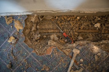 Bir dairede kırık su borusu. Yerde fayanslar, eski beton ve döküntülerle görülebilir bir delik. İnşaat alanı, evdeki su sızıntısını gidermeye çalışırken duvarda boru ve kapakçık var.