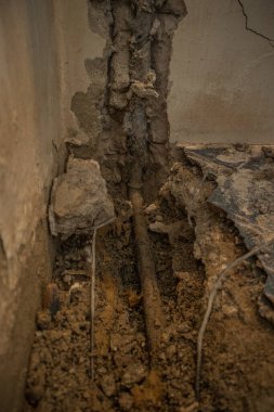 Bir dairede kırık su borusu. Yerde fayanslar, eski beton ve döküntülerle görülebilir bir delik. İnşaat alanı, evdeki su sızıntısını gidermeye çalışırken duvarda boru ve kapakçık var.