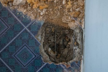 Bir dairede kırık su borusu. Yerde fayanslar, eski beton ve döküntülerle görülebilir bir delik. Evde su sızıntısını gidermeye çalışırken inşaat alanında.