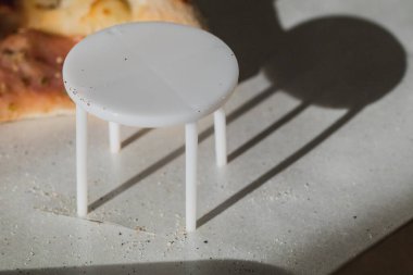 Dört ayaklı beyaz plastik pizza koruyucusu. Pizzanın karton pizza kutusunda ezilmesini önlemek için plastik bir masa. Aynı zamanda pizza masası, pizza taburesi, paket koruyucu, pizza meme ucu ya da kanepe olarak da bilinir.