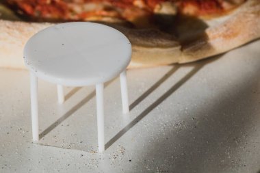 Dört ayaklı beyaz plastik pizza koruyucusu. Pizzanın karton pizza kutusunda ezilmesini önlemek için plastik bir masa. Aynı zamanda pizza masası, pizza taburesi, paket koruyucu, pizza meme ucu ya da kanepe olarak da bilinir.